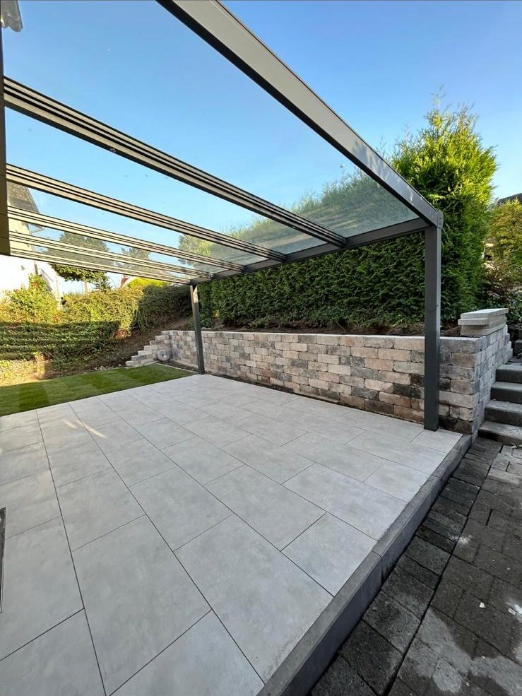 Neu gebaute Terrasse mit großformatigen Platten, Natursteinmauer und Glasüberdachung